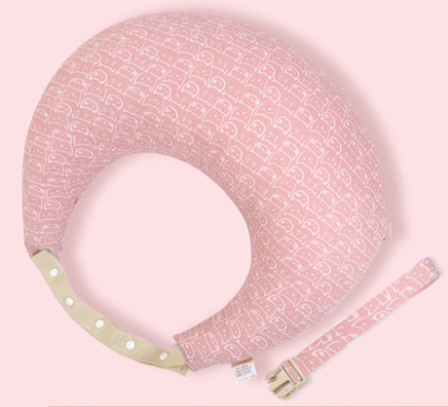 Pink nursing pillow with a whimsical white pattern on a pale pink background. It includes a beige adjustable strap with white buttons and a separate matching strap.
