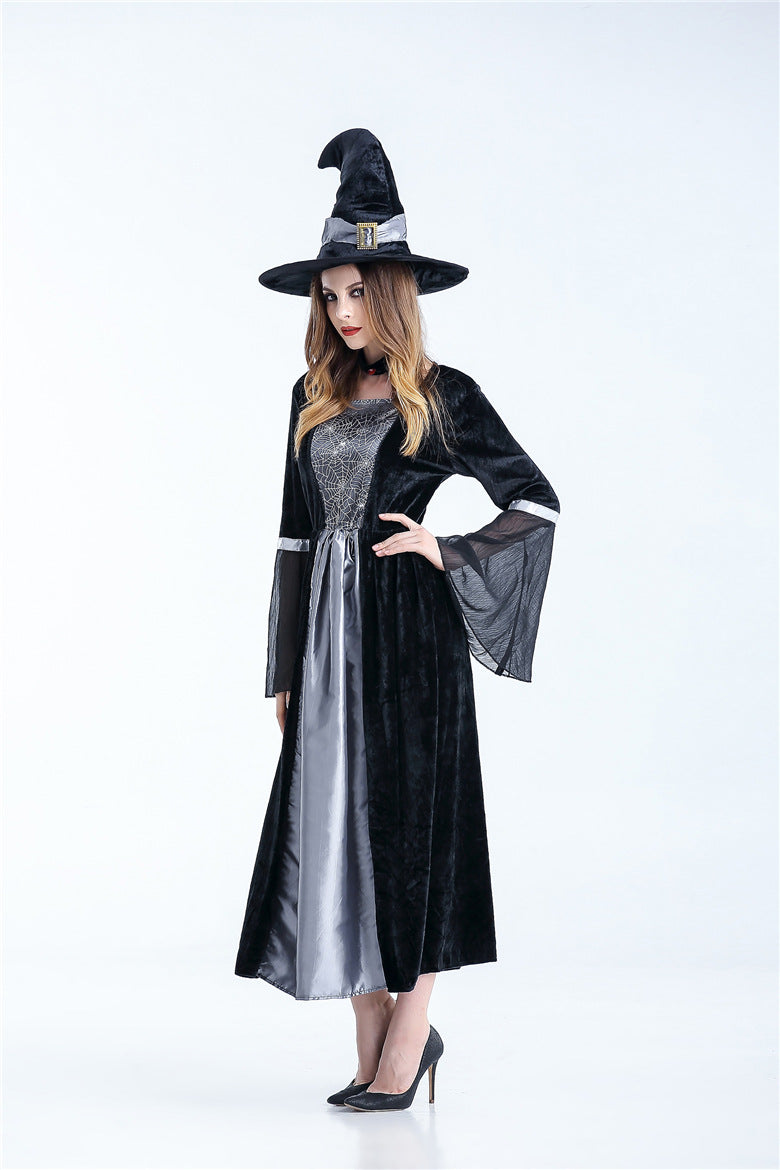 Woman in a black witch costume with a tall hat and sheer sleeves, wearing a gray and silver dress, posing against a plain white background.