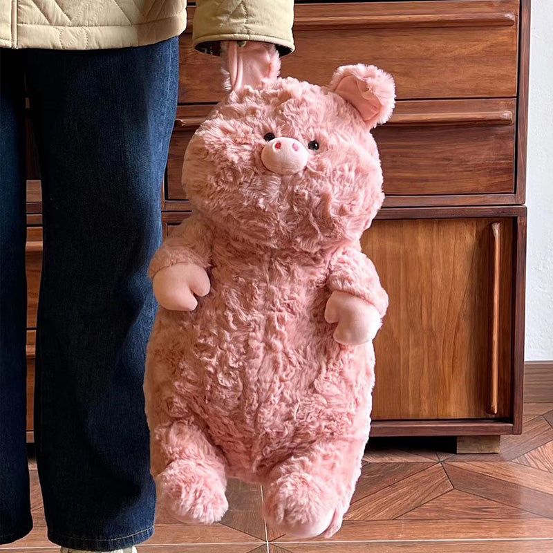 A person holding a plush pink pig with large ears and a rounded body, standing in front of a wooden dresser. The pig has a cute expression and soft texture.