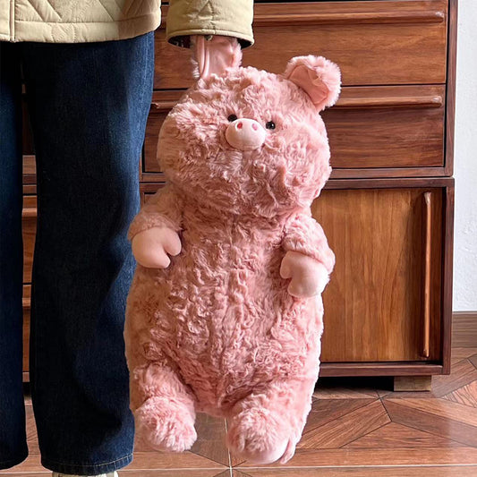 A person holding a plush pink pig with large ears and a rounded body, standing in front of a wooden dresser. The pig has a cute expression and soft texture.