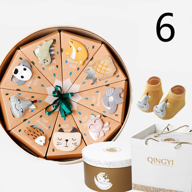 Gift set featuring animal-themed cardboard slices in a round box with a green bow. Includes a pair of yellow baby socks and a white branded gift bag.