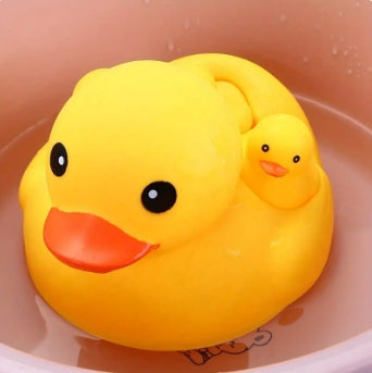 Yellow rubber duck with a smaller duck on its back, floating in a peach-colored basin. Both ducks have orange beaks and black eyes, creating a playful, cheerful appearance.