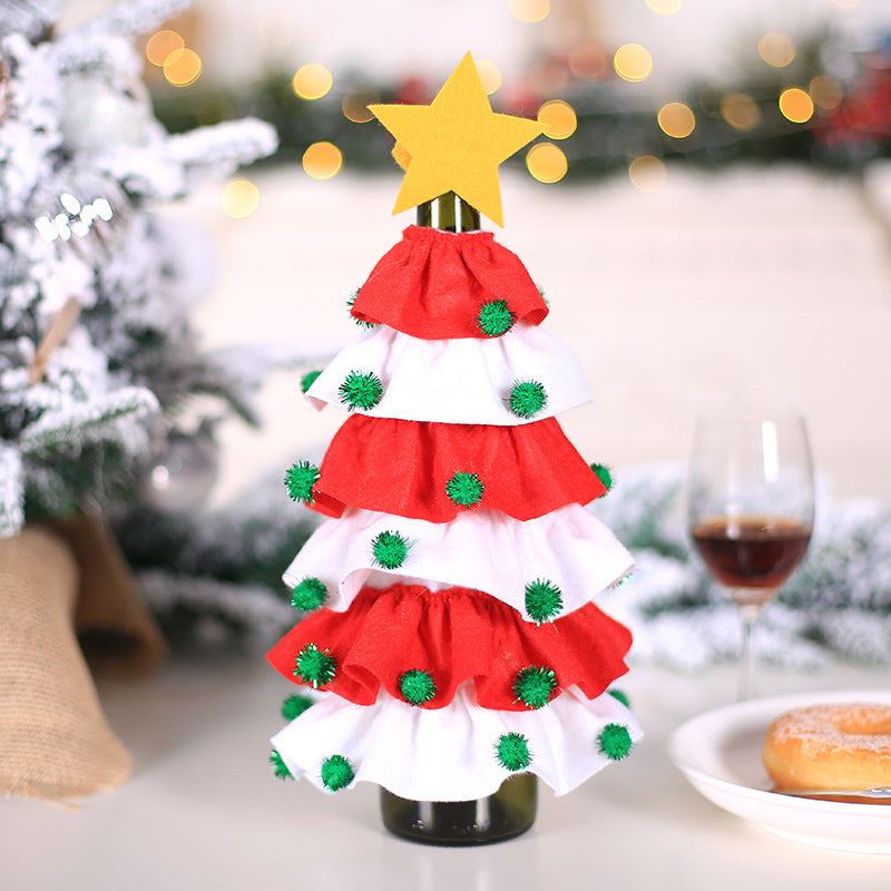 Festive tabletop Christmas tree made of red and white fabric ruffles adorned with green pom-poms, topped with a yellow star, next to wine and a donut on a snowy setting.