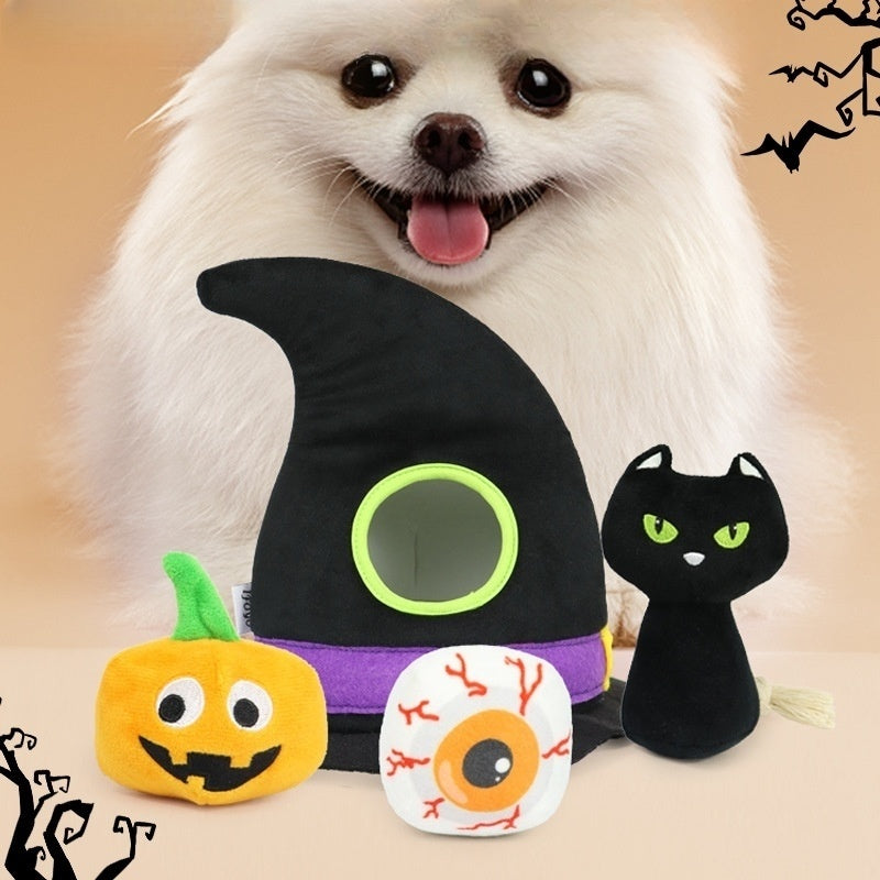 Fluffy white dog with tongue out behind Halloween-themed toys: a witch's hat with a hole, a pumpkin, a black cat, and an eyeball adorned with vines.