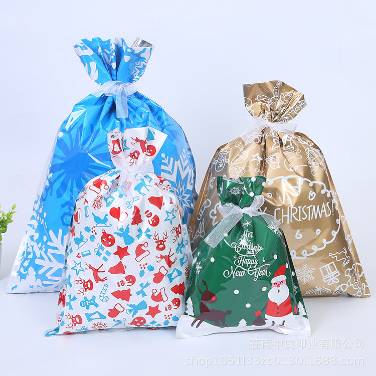 Three festive gift bags: blue with snowflakes, white with red and blue holiday motifs, and gold with "Merry Christmas" text. A small green bag features Santa and a reindeer.