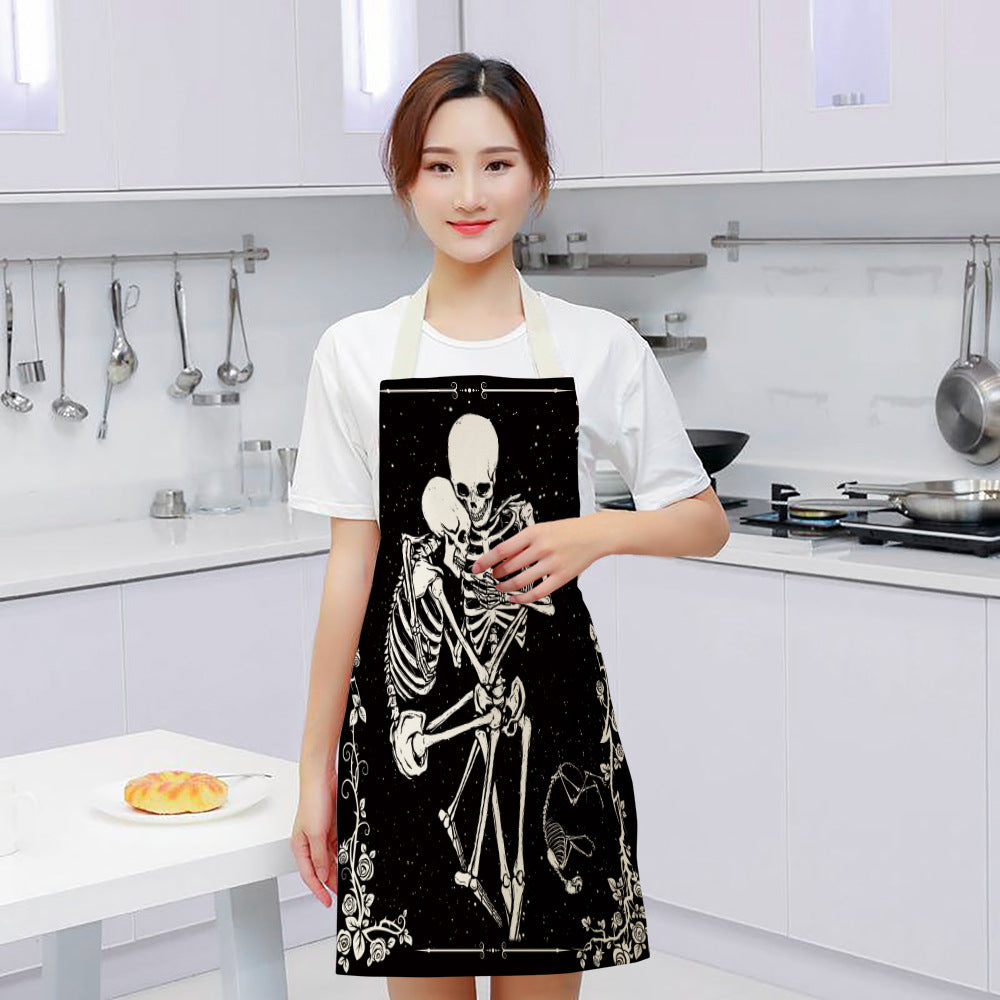 A woman in a white kitchen wearing a black apron with a skeleton design, standing near a table with a pastry and utensils hanging on the wall.