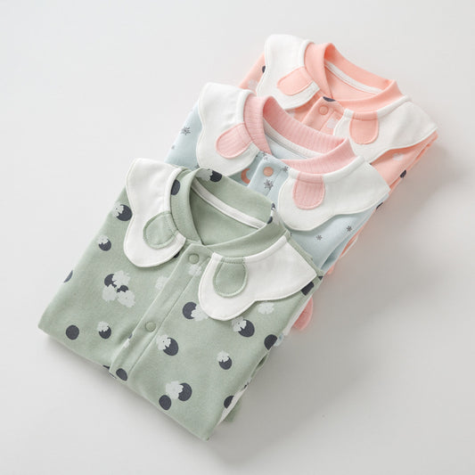 Three folded baby onesies in green, blue, and pink with playful patterns. Each has a white collar and matching neckline, stacked neatly on a white surface.