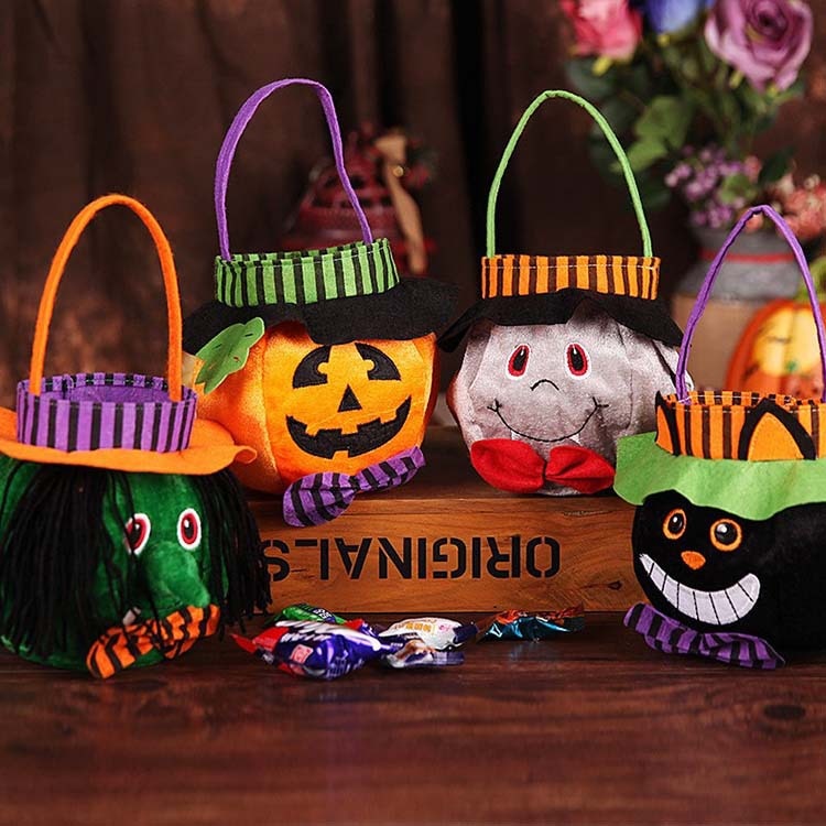 Colorful Halloween treat bags shaped like a witch, pumpkin, ghost, and cat, with fabric handles and decorations, are displayed on a wooden surface with candy scattered nearby.