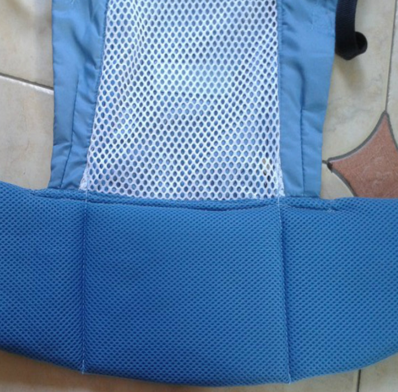 Close-up of a blue fabric with white mesh overlay and additional blue padding, set against a tiled floor background. The mesh is centered, bordered by solid blue sections.