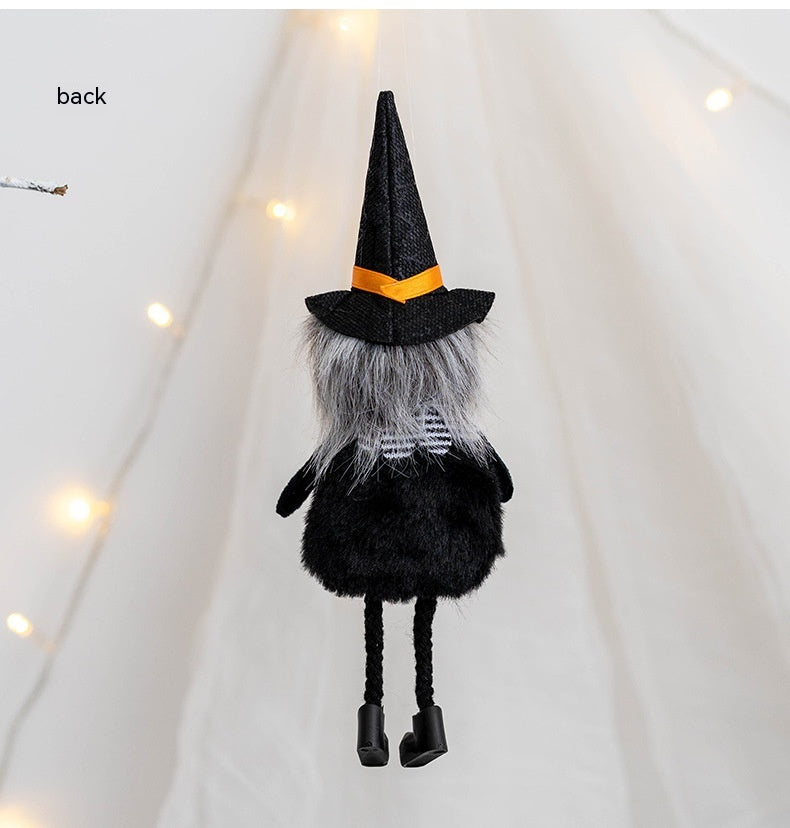 Back view of a whimsical gnome figurine wearing a black witch hat with an orange ribbon, shaggy gray hair, and black clothes. Twinkling lights softly glow in the background.