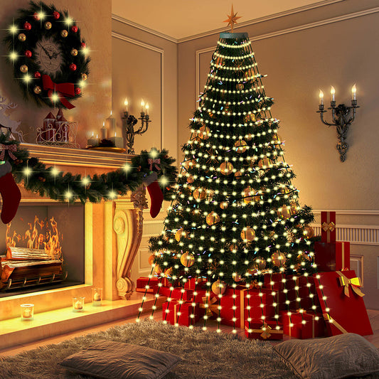 Cozy holiday scene with a decorated Christmas tree, red and gold ornaments, and wrapped gifts by a lit fireplace. A wreath and stockings hang on the mantel, illuminated by candles.