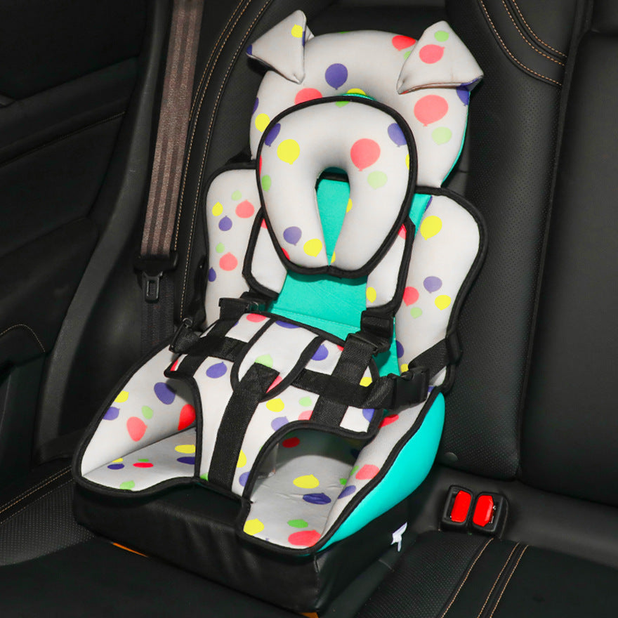 Child car seat with colorful polka dots and black straps, secured in a vehicle's rear seat. The seat has a teal cushion and a high back with playful ears.