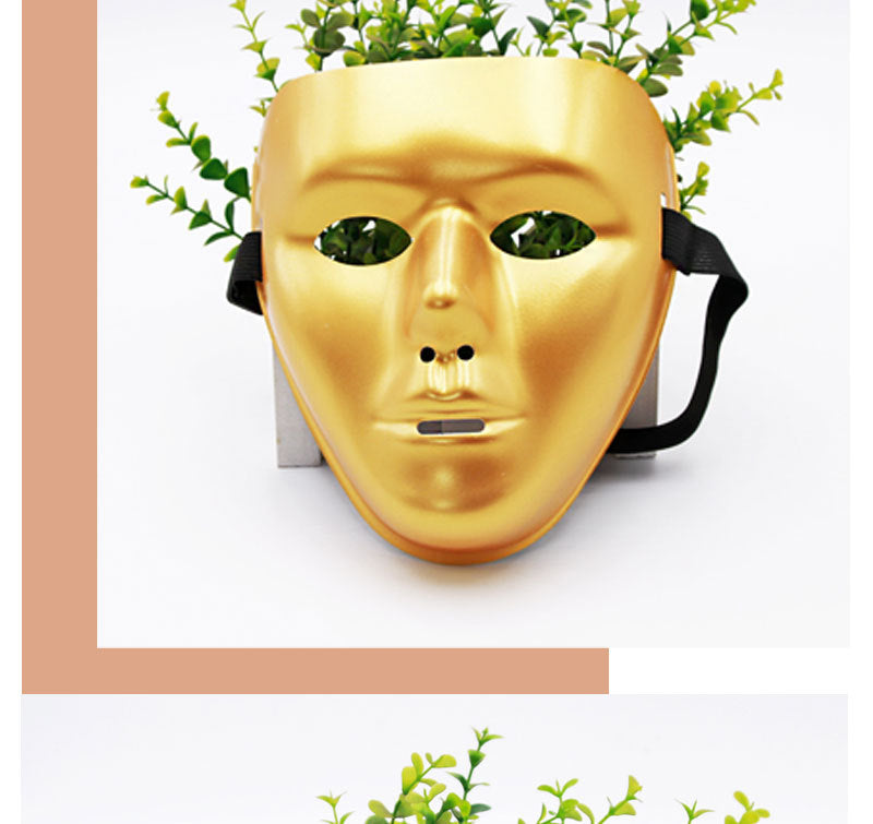 A gold mask with holes for eyes and a mouth, placed against a white background. Green plants are visible behind the mask, giving an impression of hair.