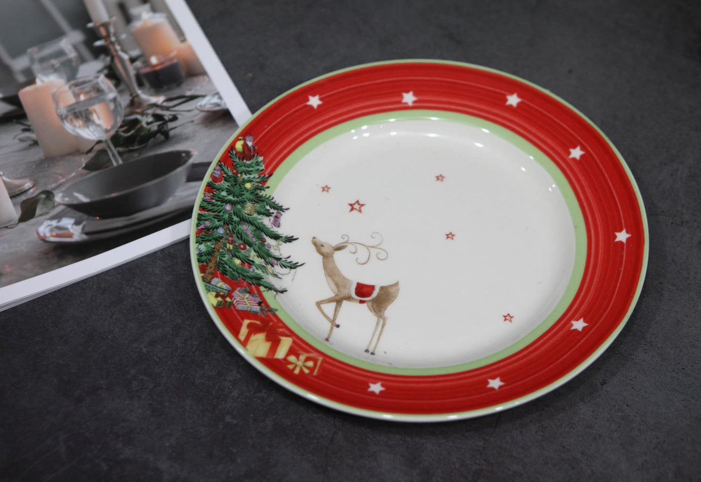 Festive plate with red border, stars, a reindeer, tree, and presents, next to a photo of a candlelit table setting with a dark bowl, glass, and white candles.