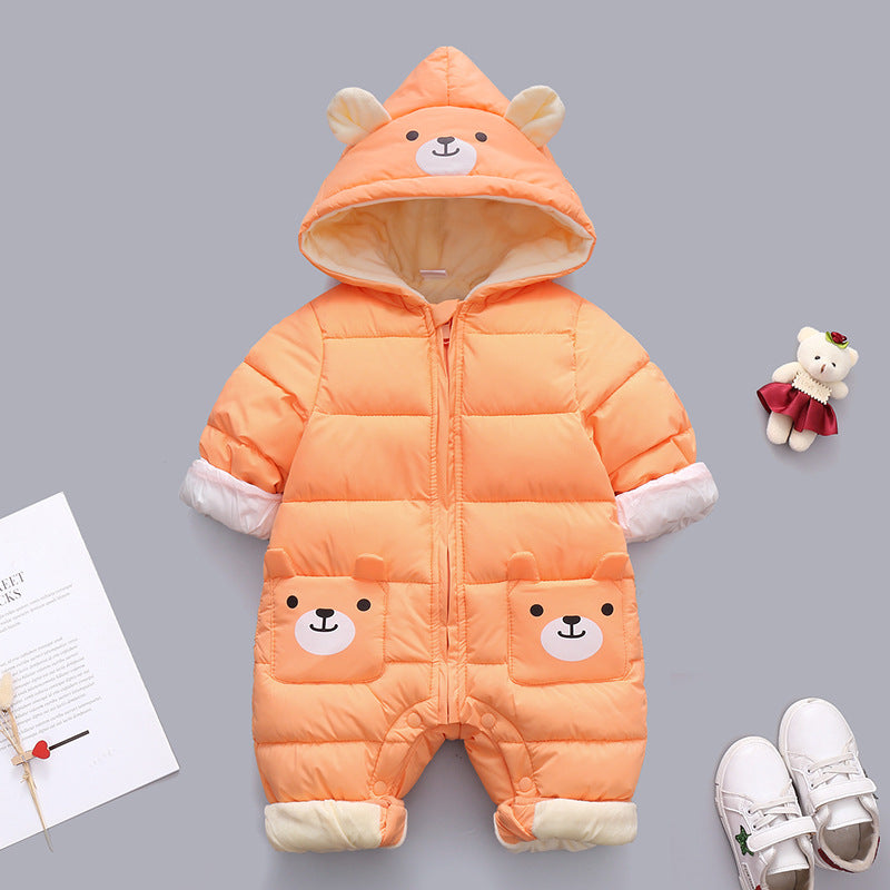 Orange baby snowsuit with bear ears and face on the hood, bear pockets, paired with white sneakers, bear plush toy, and a decorative paper on a grey background.