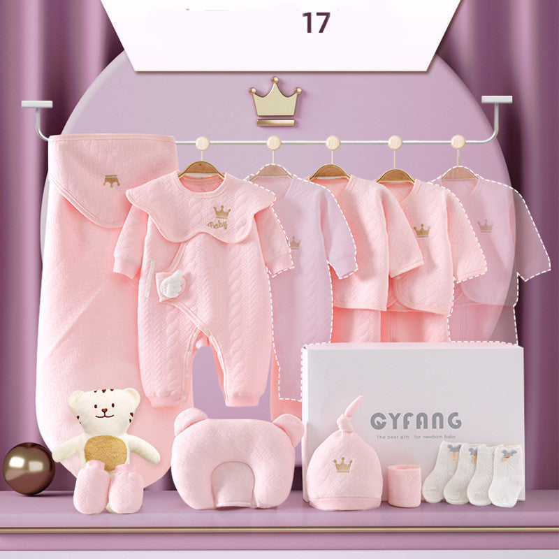 A set of pink baby clothes and accessories on display. Includes onesies, a swaddle, socks, a hat, and a plush toy. The items are decorated with small crown motifs.