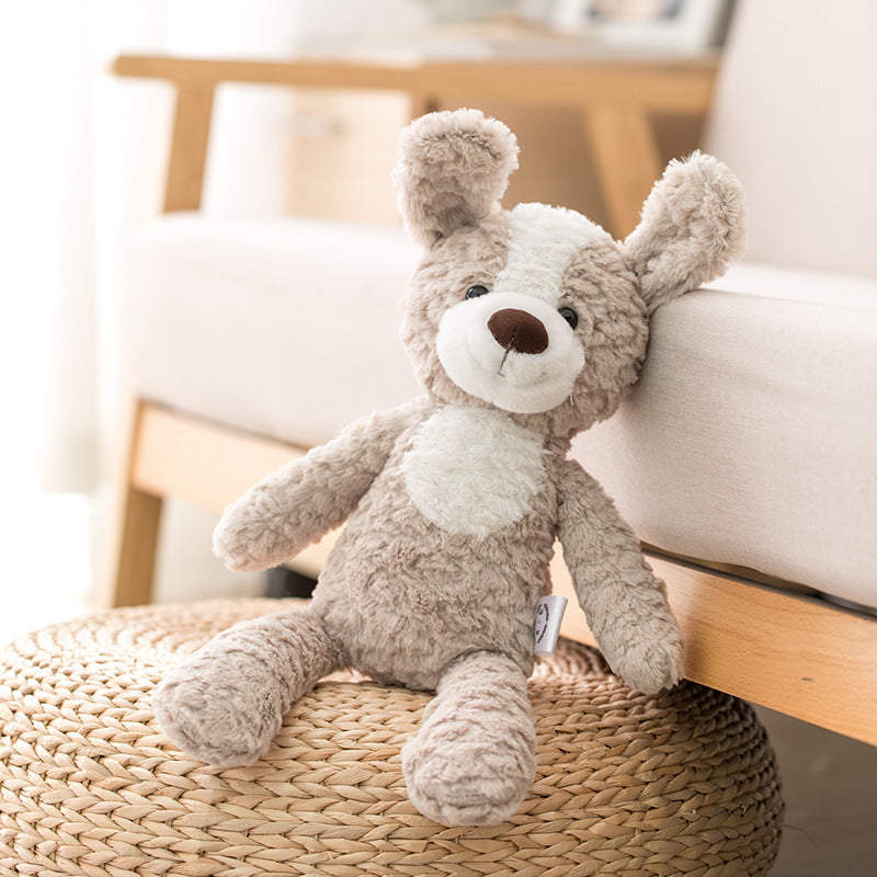A cuddly, gray and white stuffed dog toy with floppy ears leans against a beige couch, sitting on a woven ottoman in a softly lit room.