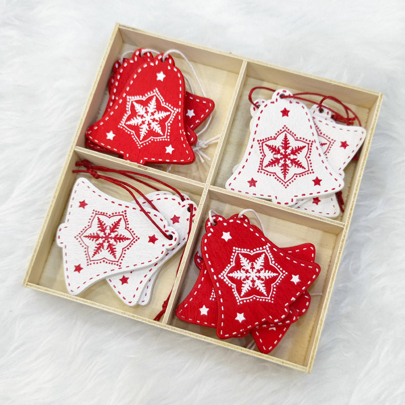 Wooden box with four sections containing red and white bell-shaped ornaments, each featuring a snowflake and star design, placed on a fluffy white surface.