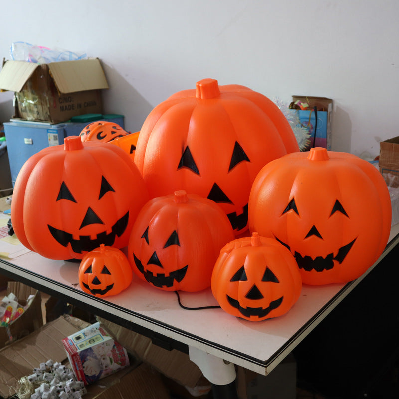 A collection of bright orange plastic pumpkins with black carved faces, varying in size, displayed on a table. Cardboard boxes and other items are visible in the background.