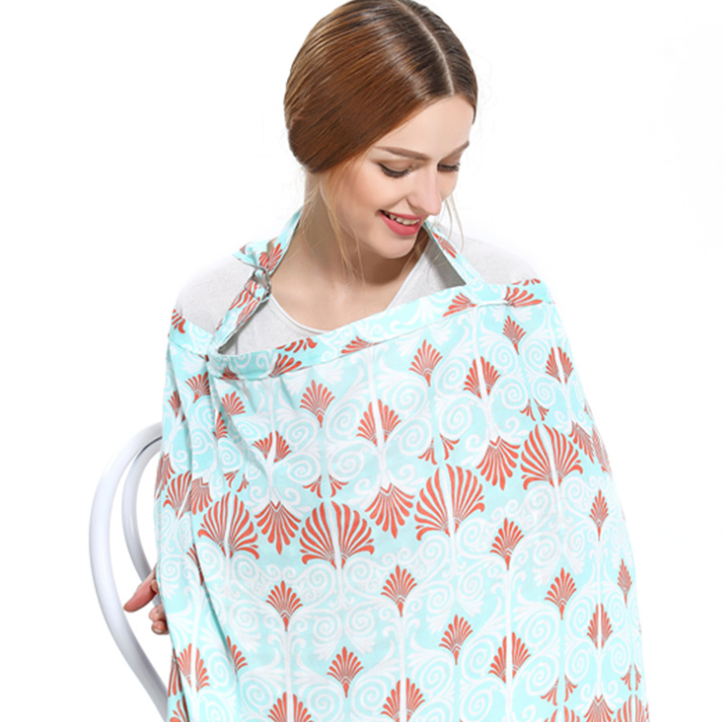Woman wearing a patterned nursing cover with orange and blue swirls sits, smiling downwards. The cover drapes around her, and she holds the fabric partially aside.