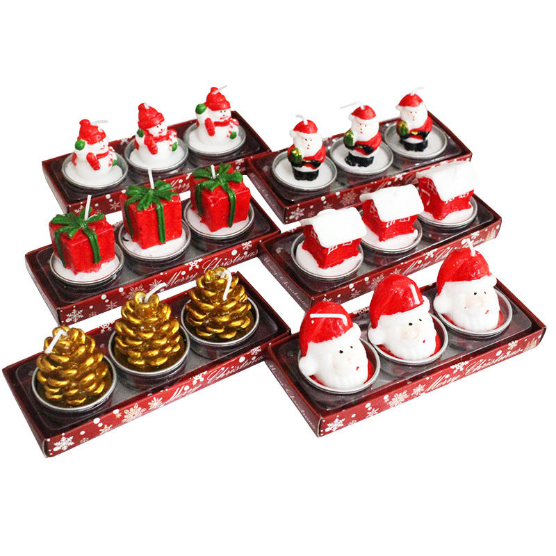 Festive candles shaped as snowmen, Santa, gifts, houses, gold pinecones, and Santa heads in red trays. Each set has matching holiday-themed designs.