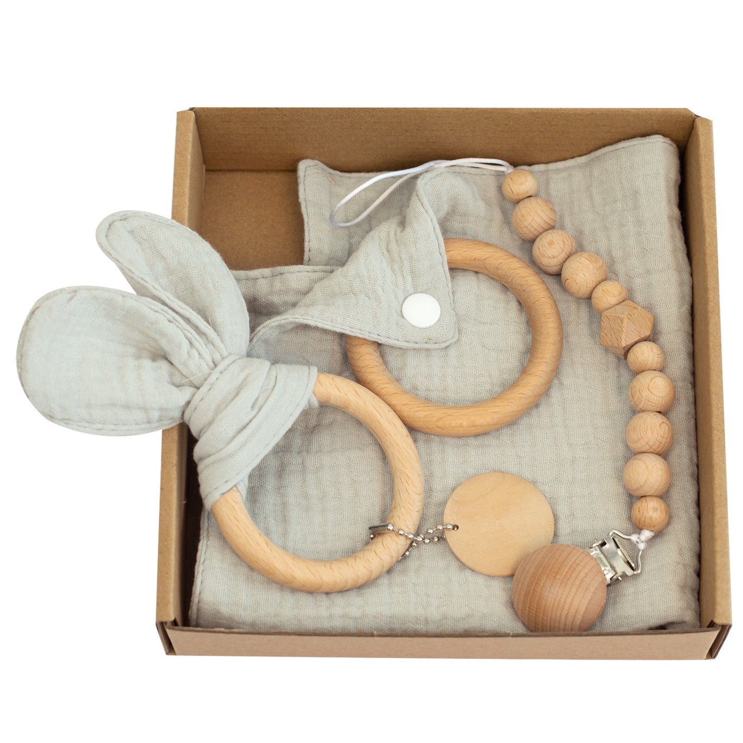 A cardboard box contains a baby gift set with wooden teething rings, a pacifier clip with wooden beads, and a soft gray cloth bib featuring a snap button.