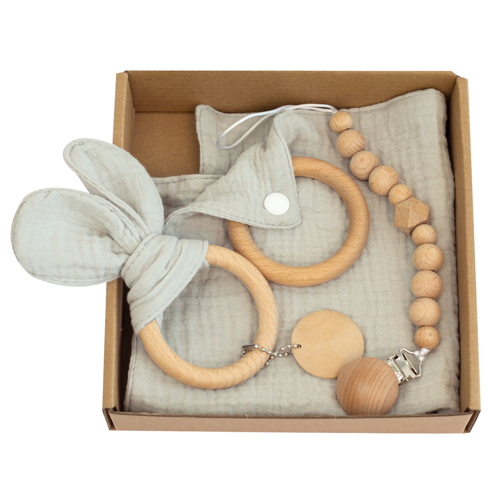A cardboard box contains baby accessories, including a wooden teething ring with soft gray ears, a pacifier clip with wooden beads, and a matching gray muslin cloth.