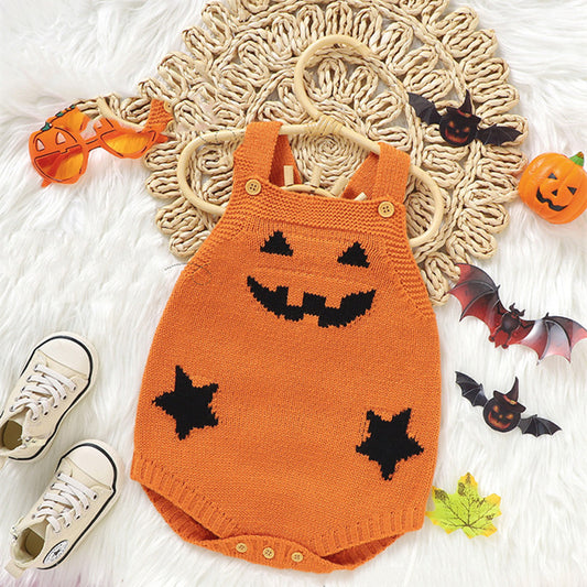 Orange knit romper with a jack-o'-lantern face and star patterns. Surrounding it are pumpkin glasses, paper bats, a toy pumpkin, baby sneakers, and decorative autumn leaves.