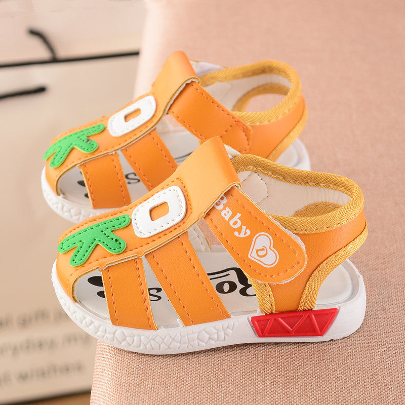 Orange toddler sandals with green leaf accents and "O" designs, featuring "baby" and heart details. They have white soles with red patches and an open-toe style.
