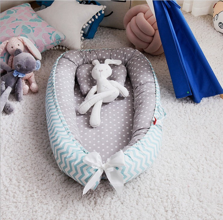 Baby nest with star pattern and chevron sides, holding a stuffed bunny toy. Surrounded by plush toys, pillows, and a blue tent, all on a soft white carpet.