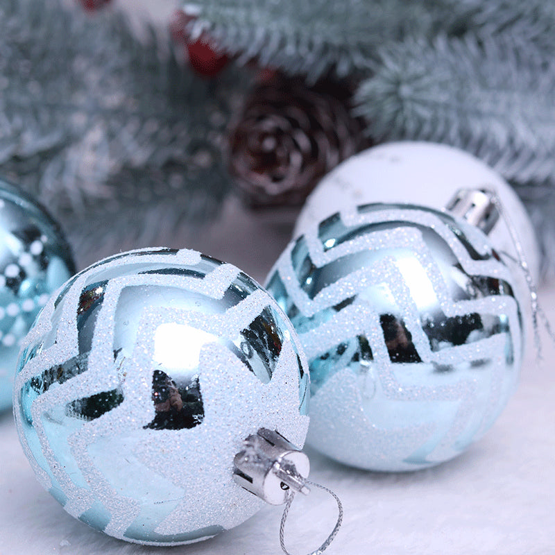 Close-up of shiny blue and white Christmas ornaments with zigzag patterns, set against a backdrop of frosted pine branches and pinecones.