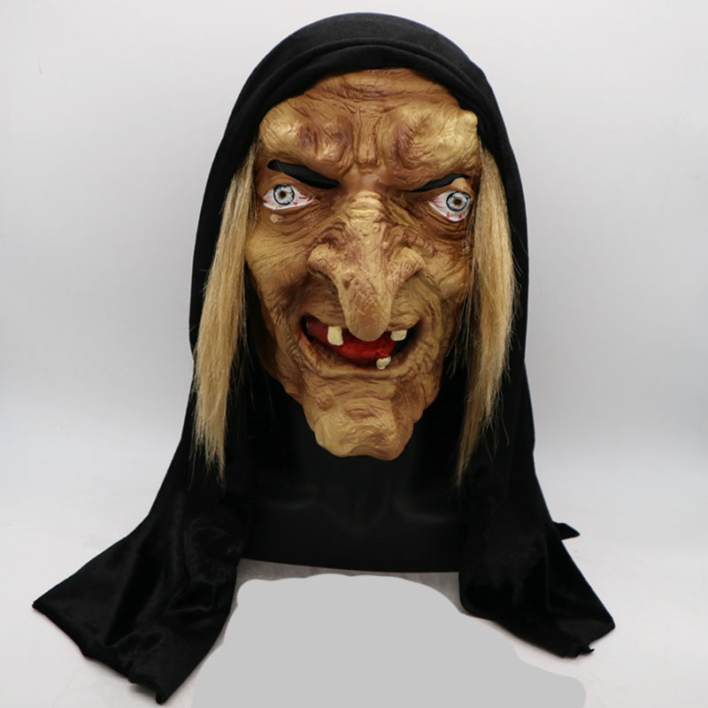 A realistic mask of a witch with exaggerated facial features, crooked teeth, and long blond hair, wearing a black hood. The eyes are wide with distinctive makeup.