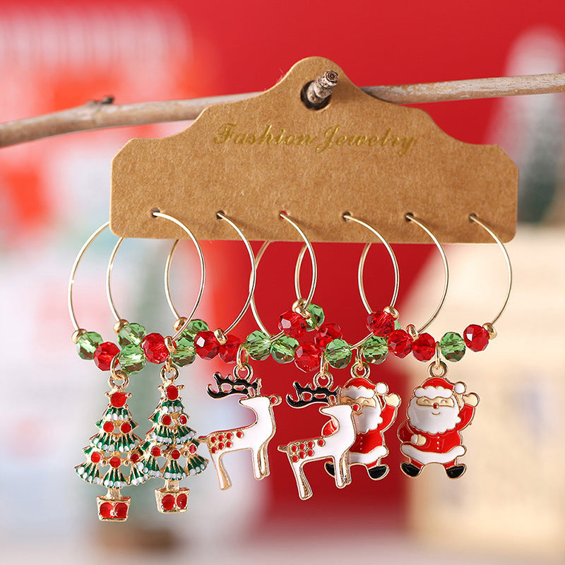 Four pairs of festive hoop earrings with red and green beads, featuring Christmas tree, reindeer, and Santa Claus charms, displayed on a card labeled "Fashion Jewelry."