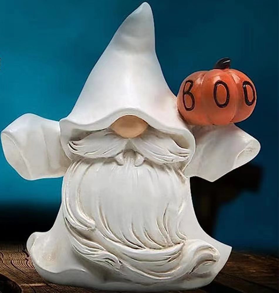 A white ceramic gnome with a bushy beard, wearing a pointed hat, holds an orange pumpkin inscribed with "BOO". The background is a deep blue, adding contrast to the figure.