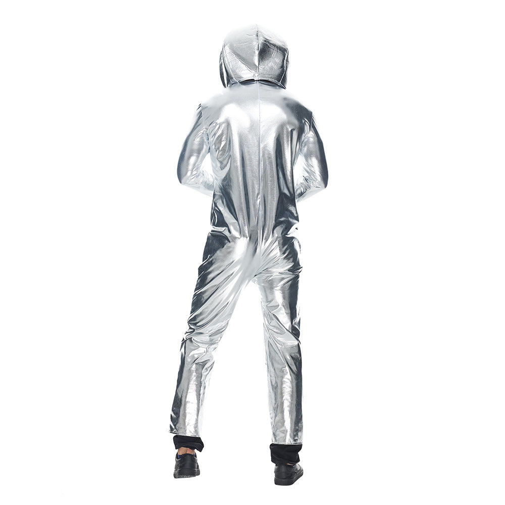 A person is standing with their back to the camera, wearing a shiny silver jumpsuit and a hood. The suit reflects light, creating a metallic effect. They wear black shoes peeking out from the suit's cuffs. The background is plain white.