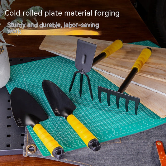 Set of gardening tools with yellow handles, including a trowel, transplanter, rake, and fork, displayed on a green cutting mat with wooden boards in the background.