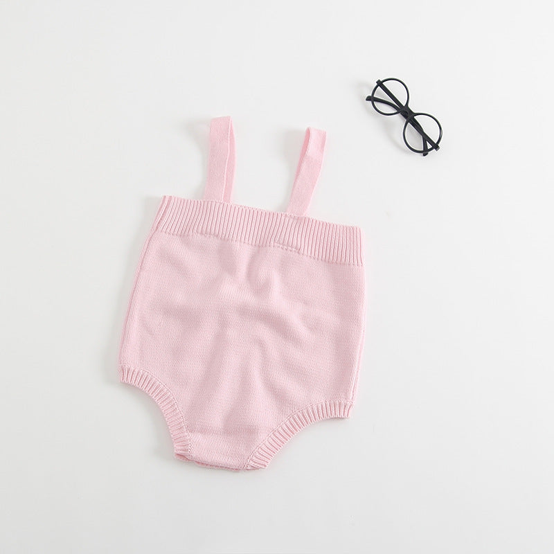 Pink knitted baby romper with shoulder straps placed on a white background. Black round glasses lie nearby.