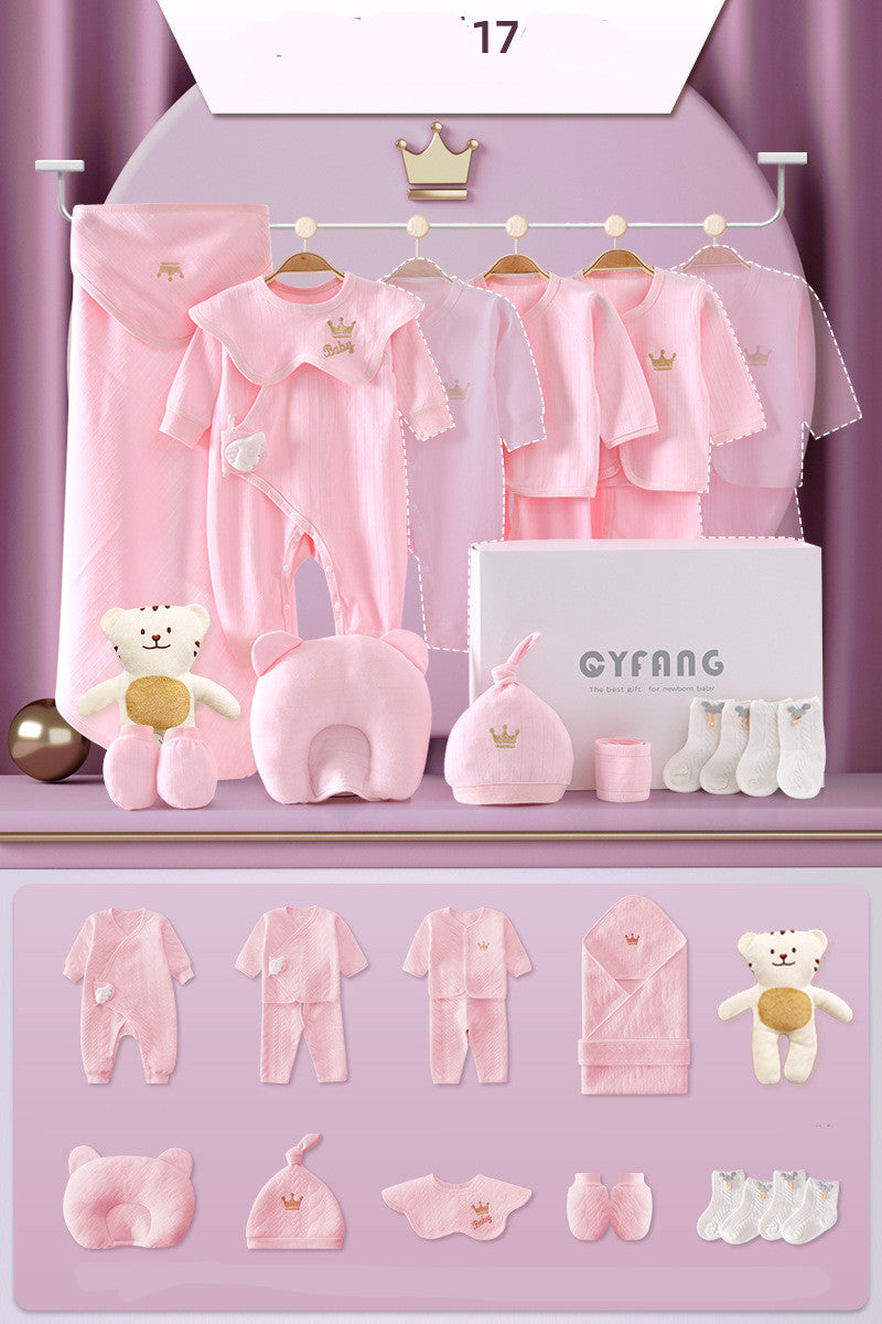 Pink baby gift set includes clothing, blanket, hat, bib, socks, and plush toys. Items are displayed on a rack and flat surface, all featuring a crown motif.
