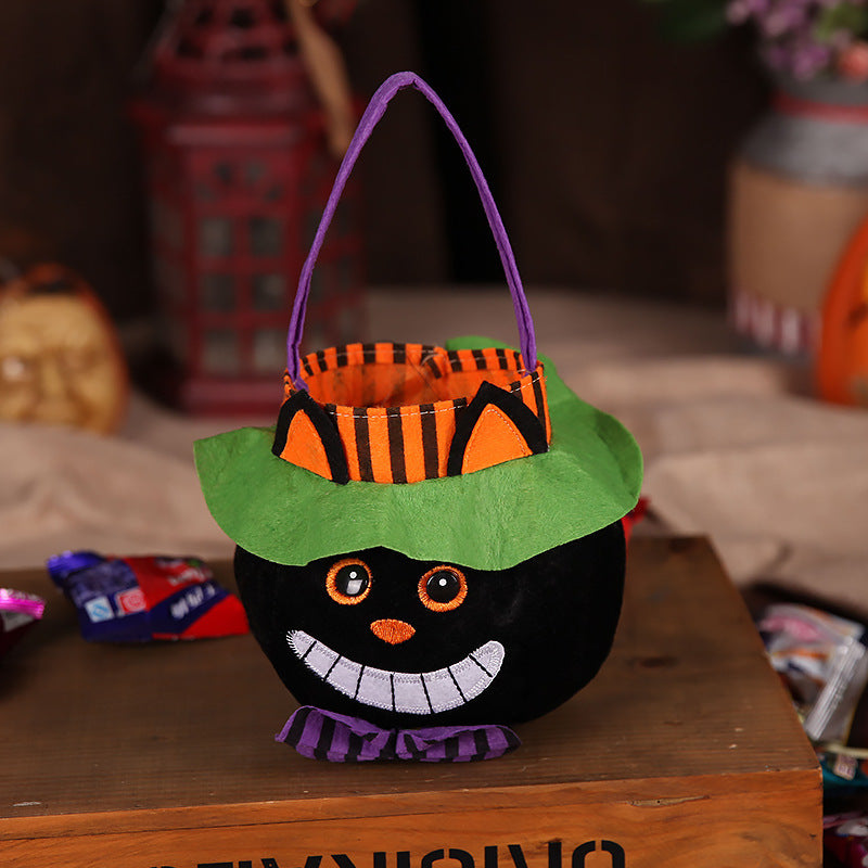A Halloween-themed basket resembling a black cat, with orange stripes, green brim, and a wide grin. It has purple handles and sits on a wooden surface, surrounded by blurred decorations.