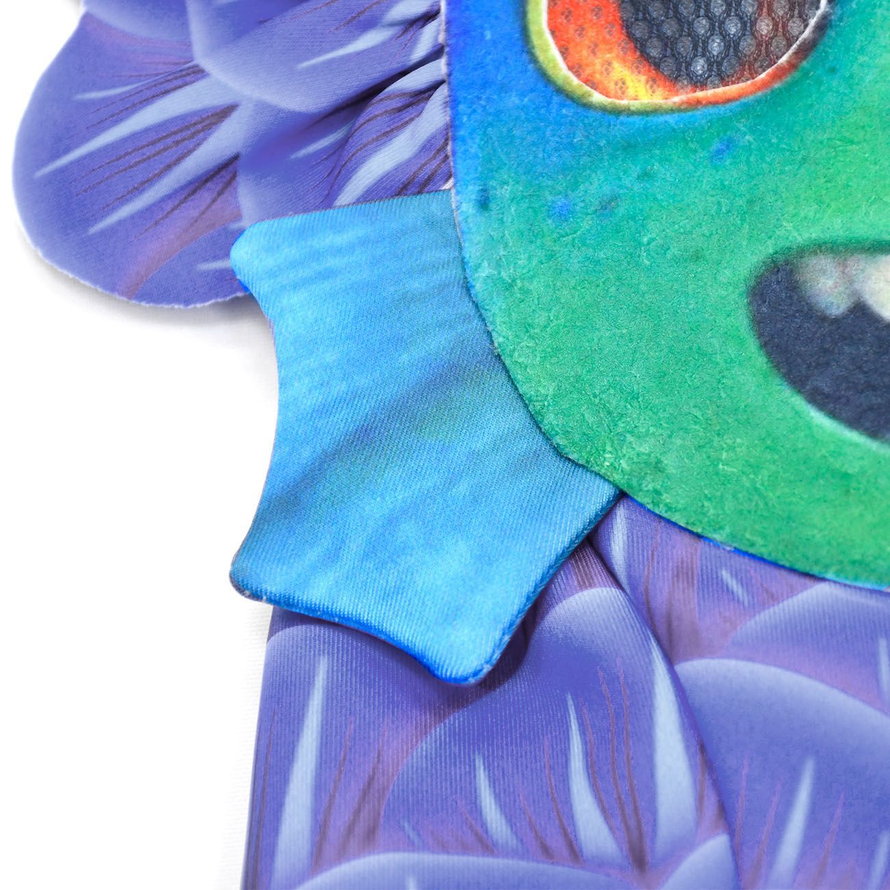 Close-up of a colorful fabric fish costume, featuring a green face with an orange eye, blue fin, and purple scale-like patterns resembling fish fins.