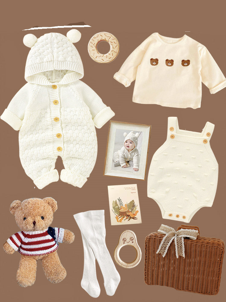 Flat lay of baby items on a brown background, including a white knit onesie with bear ears, a bear-patterned shirt, romper, white socks, a teddy bear, wicker basket, photo, and toys.