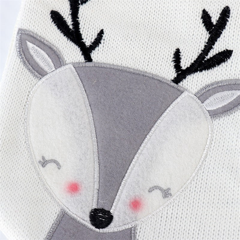 Close-up of a cute reindeer face design on a knitted fabric. The reindeer has a grey face, pink cheeks, and black antlers, with embroidered eyes and a nose.