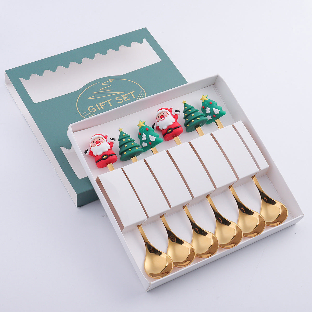 Gift set box with six gold spoons. Handles feature festive designs: Santa Claus and Christmas trees. The open box is green with a decorative window and "Gift Set" text.