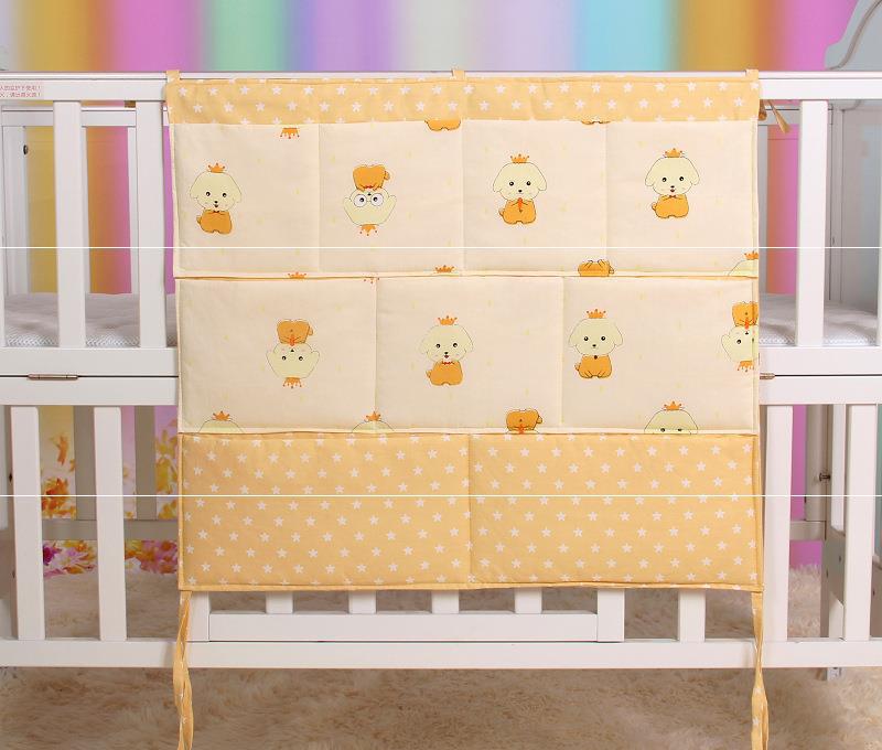 Yellow crib organizer with star and cartoon animal patterns hangs on a white crib. The background features a blurred, multicolored wall.