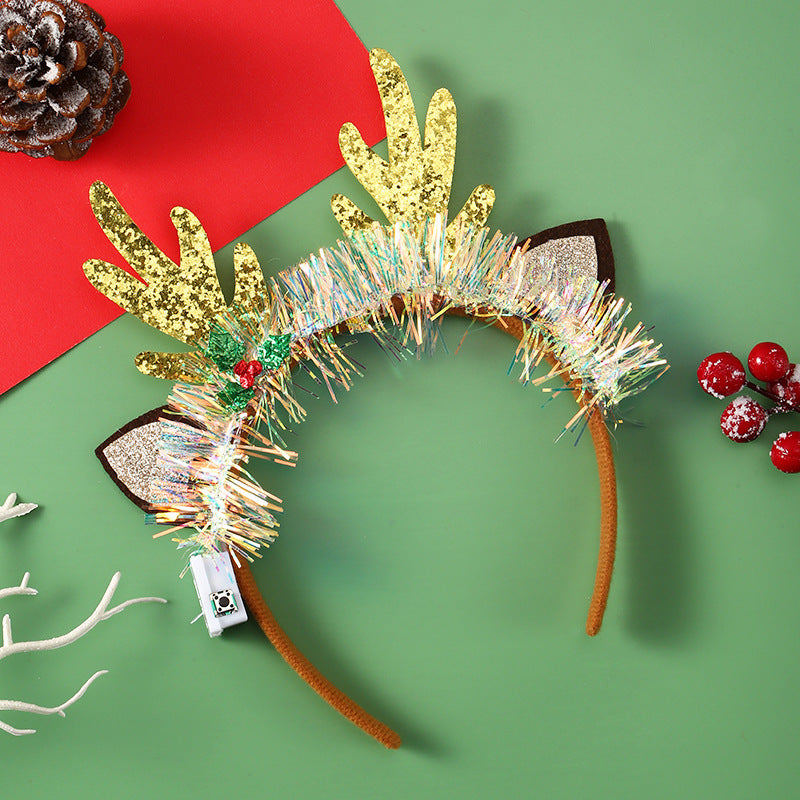 Festive reindeer antler headband with gold glitter antlers, tinsel decor, and holly accent on a green and red background, bordered by a pinecone and frosted berries.