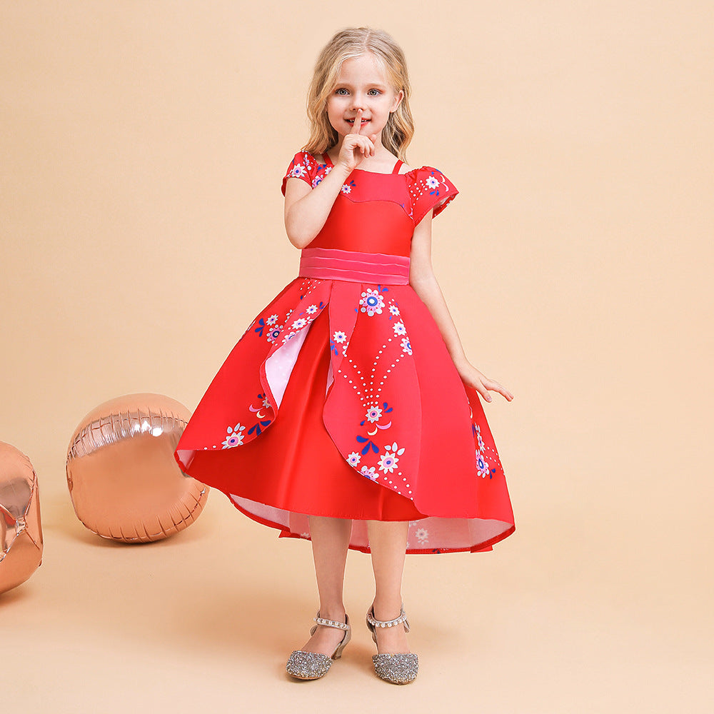 Young girl in a red floral dress stands against a beige background. She gestures with a finger to her lips, with rose-gold balloons beside her. Silver shoes complete the outfit.