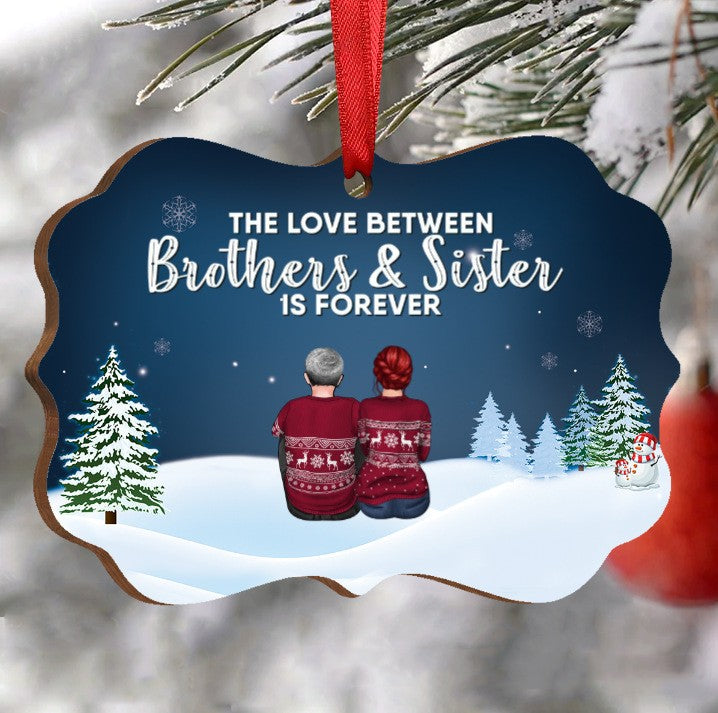 Holiday ornament with two people in festive sweaters on a snowy scene, surrounded by trees. Text reads, "The love between brothers & sister is forever."