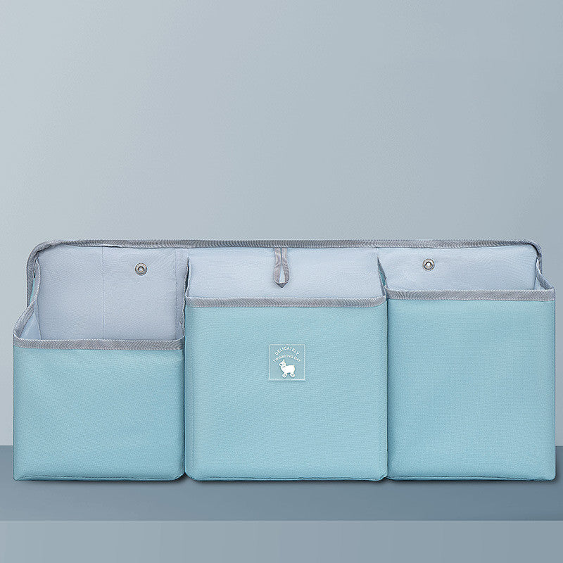 A light blue three-pocket organizer with gray trim, featuring a decorative logo on the front. It is set against a matching blue background, showcasing its compact design.