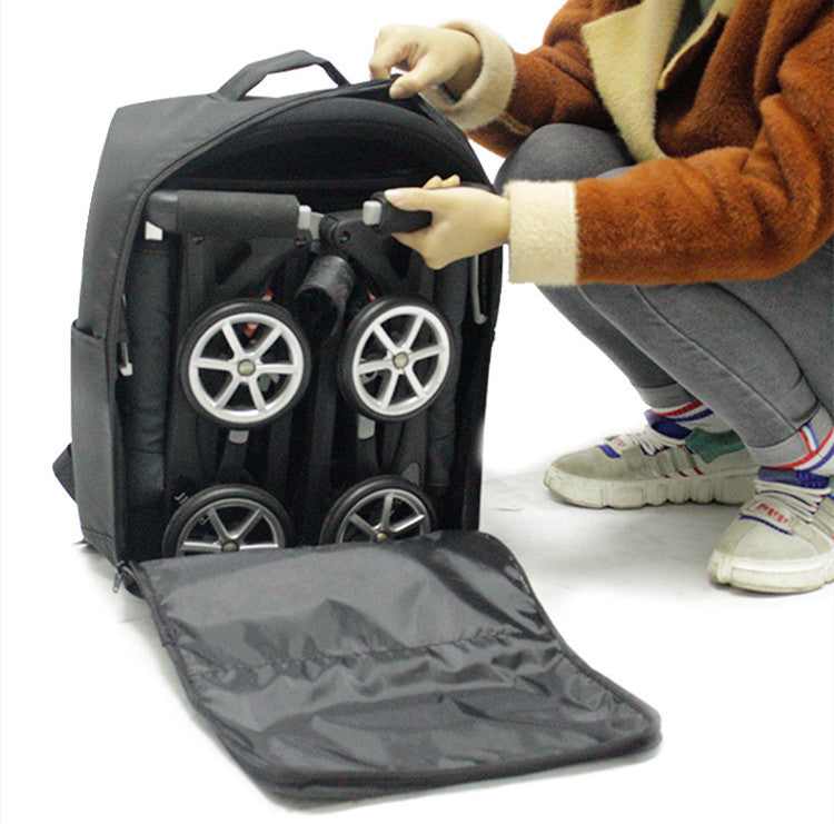 A person is kneeling next to an open black backpack revealing a folded stroller with wheels inside. The backpack has a handle on top and a flap opening at the front.