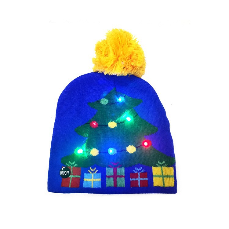 Blue beanie with a yellow pom-pom featuring a lit-up Christmas tree design and presents. The tree has colorful LED lights, and a small on/off button is visible.